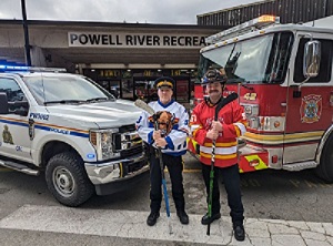A police officer dressed in a hockey jersey standing in front of a police car and a firefighter dressed in a hockey jersey standing in front of a fire truck