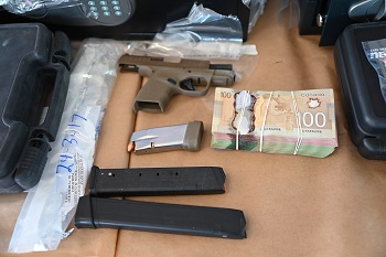 Trois chargeurs de cartouches, une arme de poing brune et une liasse de monnaie canadienne se trouvent sur une table.