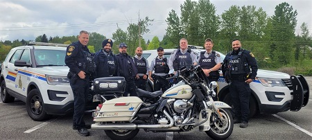 Photo of police officers standing in front of police cars and a police motorcycle