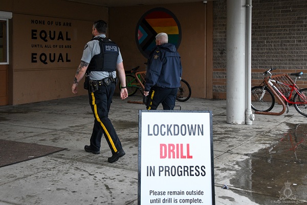 RCMP officers walking into a school to conduct a lockdown drill. In front of them is a sign that reads "Lockdown Drill in Progress"