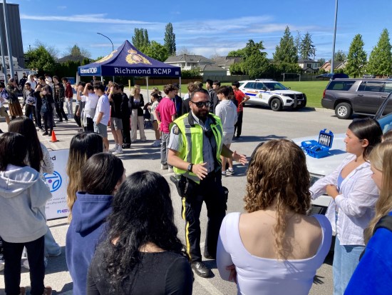 RCMP officer having a conversation with a group of secondary students outdoors