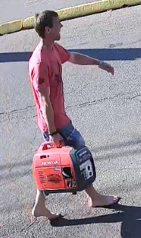 suspect wearing a red t-shirt and blue knee length baggy shorts with several wide horizontal stripes. He is not wearing shoes, has short brown hair, and is carrying the stolen generator.