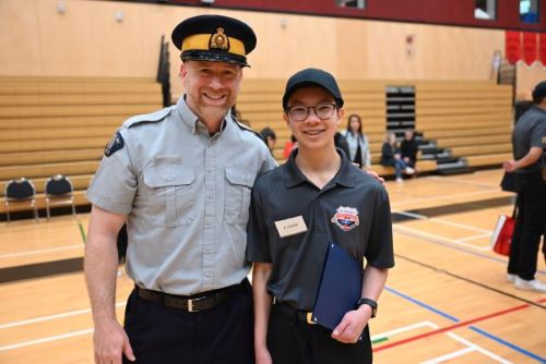 Un agent en uniforme de la GRC se tient à côté d’un adolescent souriant dans le gymnase d’une école