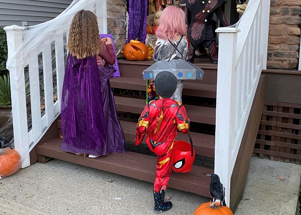 Three children dressed as a witch, alien and superhero walking up stairs while trick-or-treating