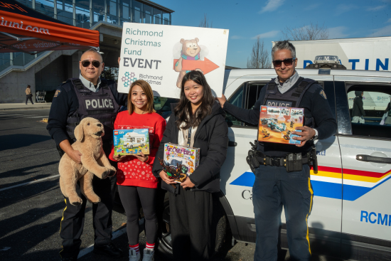 Des policiers de la GRC de Richmond et des bénévoles tiennent des jouets devant un véhicule de police