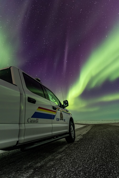 RCMP Pick up truck parked on snowy gravel road with the Northern Lights in the sky. 