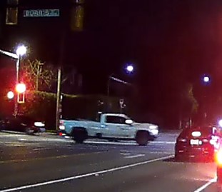 White pickup truck driving through an intersection with several other vehicles stopped at the red light.