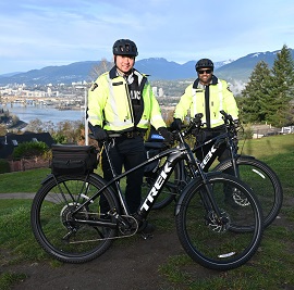 Two police officers in reflective jacket stand with E-Bikes in front of them and mountains in the background 