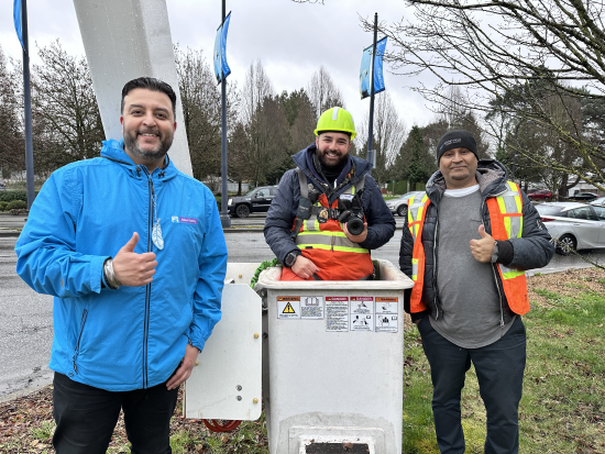 2 men giving a thumbs up sign standing on either side of a man in an aerial bucket holding a camera