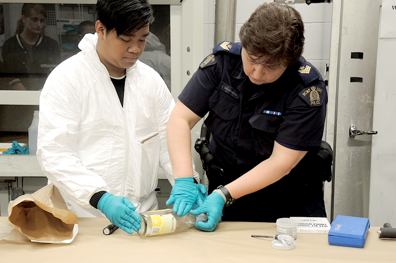 Police Academy participant conducts a mock forensic examination of a bottle alongside an Forensics police officer.