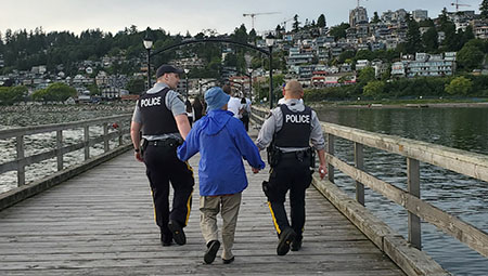 two officers holding hands of a civilian walking down pier