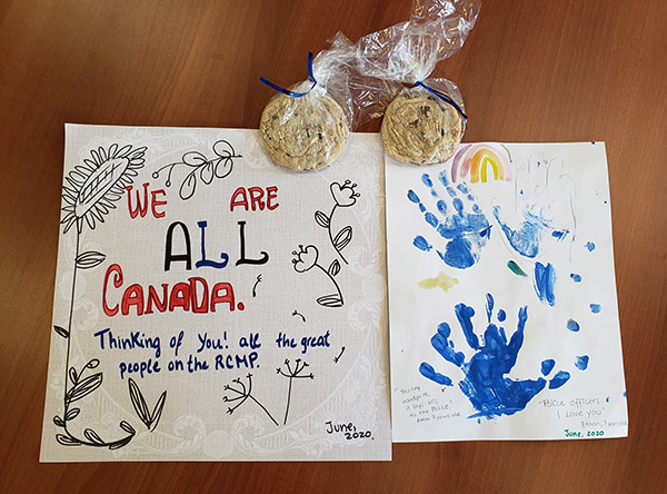 Deux cartes écrites à la main et deux sacs de biscuits faits maison. Des fleurs sont dessinées sur l’une des cartes, alors que des empreintes de mains bleues et un arc-en-ciel figurent sur l’autre.