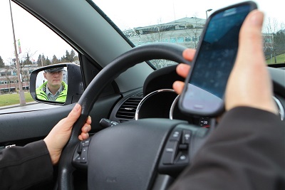 Un conducteur tient un téléphone cellulaire dans sa main droite et un agent de police observe l’infraction.