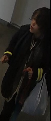 Personne aux courts cheveux noirs qui porte une veste de BC Ferries, un gilet réfléchissant de l’entreprise Bee-Clean, un pantalon foncé et des chaussures noires. Elle transporte également un sac en plastique blanc.