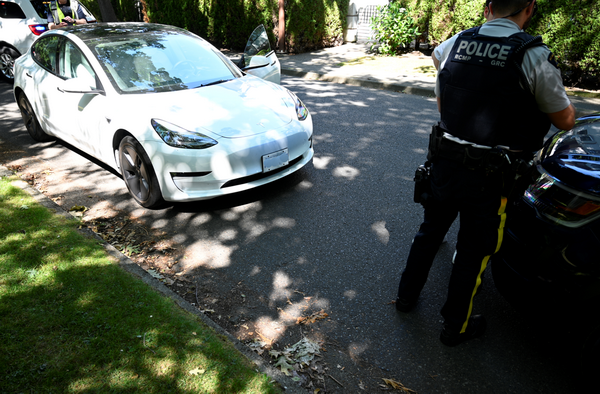 Photo d’un agent de police se tenant à côté d’une voiture blanche qui fait l’objet d’une enquête sur une opération présumée d’exploitants sans permis de services de voiturage.