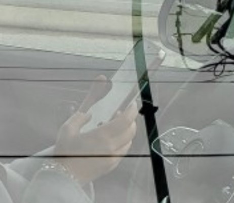 Two hands on a phone inside a car near a steering wheel
