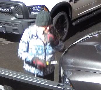 Photo tirée de la vidéo montrant la suspecte s’approchant d’un véhicule; elle porte des gants, un chandail bleu et blanc et retire son masque