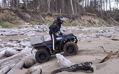 Member on ATV on a beach with driftwood