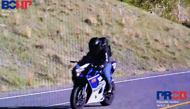 Photo of man in a black motorcycle helmet with black visor obscuring his face, riding a blue and white Suzuki motorcycle.