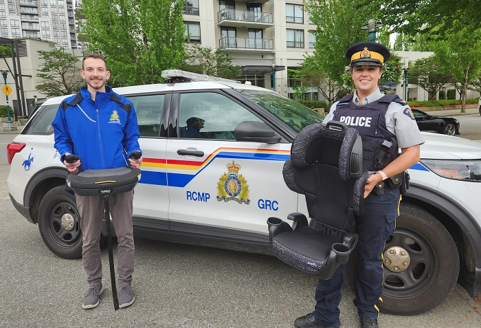 Un employé de la ville de Coquitlam et un agent de la GRC tiennent des sièges d’auto devant un véhicule de police identifié.