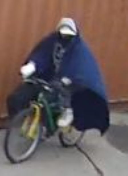 Suspect leaning over: A person in a grey hoodie and blue pants leans over in front of a tire pile and tends to a black bag. His pants are falling down slightly. A green and yellow bike is beside him with a blue blanket draped over top. A white bulky glove or cast is on his right hand and forearm. 