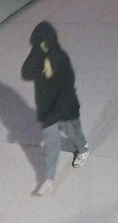 Une jeune suspecte qui porte un chandail foncé à capuchon et des chaussures de course Nike. On voit possiblement ses cheveux blonds.