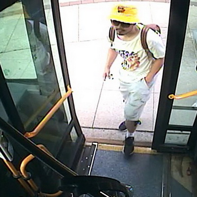 Photo de Ryan Liu qui monte dans un autobus et qui porte un short vert, un tee-shirt blanc, des chaussures noires et un chapeau jaune
