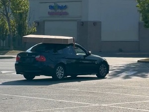 black BMW with stolen 75-inch television balanced on top of the vehicle