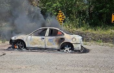 burned out car on the side of the road with smoke rising from the cabin area