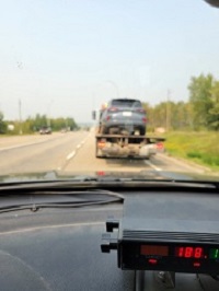 Vue à travers le pare-brise d’une voiture de police avec un radar à l’avant-plan et un véhicule sur une remorqueuse à l’arrière-plan.