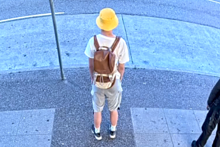 Photo de Ryan Liu debout dans la rue, alors qu’il porte un short beige, t-shirt blanc, des souliers noirs, un chapeau jaune et un sac à dos marron