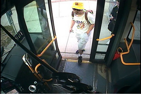 Photo de Ryan Liu qui monte dans un autobus et qui porte un short beige, un t-shirt blanc, des souliers noirs et un chapeau jaune