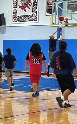 Photo of youth playing basket ball watching as  RCMP Cpl GROSS making a basket