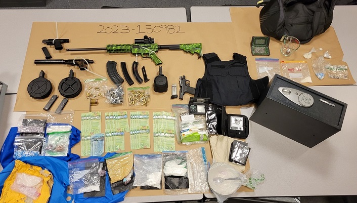 Photo d'armes à feu, d'espèces en billets de 20 dollars, de sacs de drogues présumées, de gilets pare-balles affichés sur une table