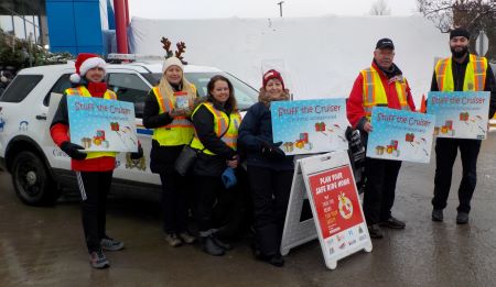 Bourrer une voiture de police : Des bénévoles de l’Équipe de la prévention du crime et des membres du personnel portant des gilets de haute visibilité rassemblés devant une voiture de police avec des affiches de l’événement Bourrer une voiture de police.