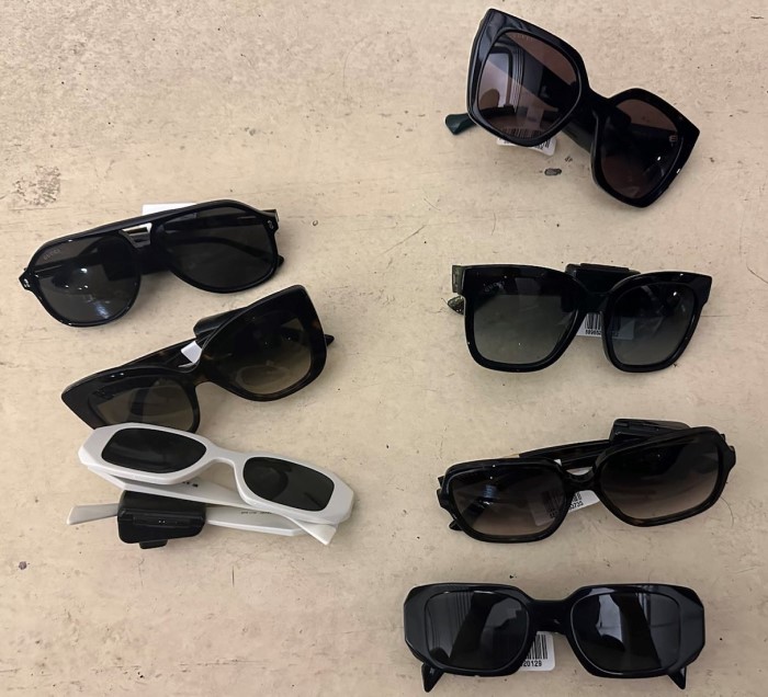 Seven pairs of sunglasses with tags on the arms sitting on a flat surface