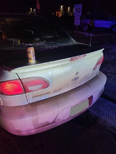 Une photo de nuit de l’arrière d’une voiture avec sur le coffre une canette de bière Coors. 