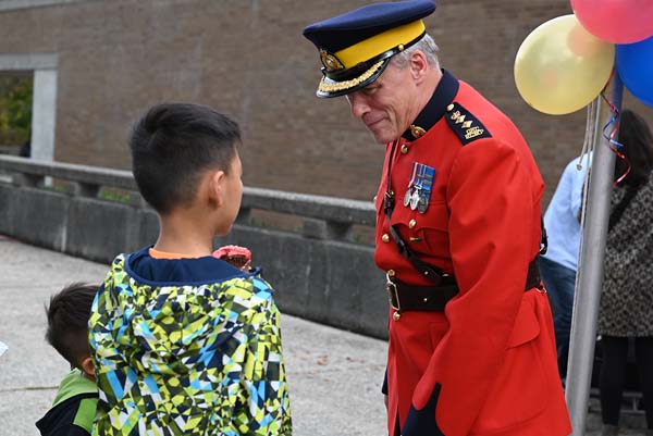 An officer in Red Serge speaks with a young boy outdoors beside balloons